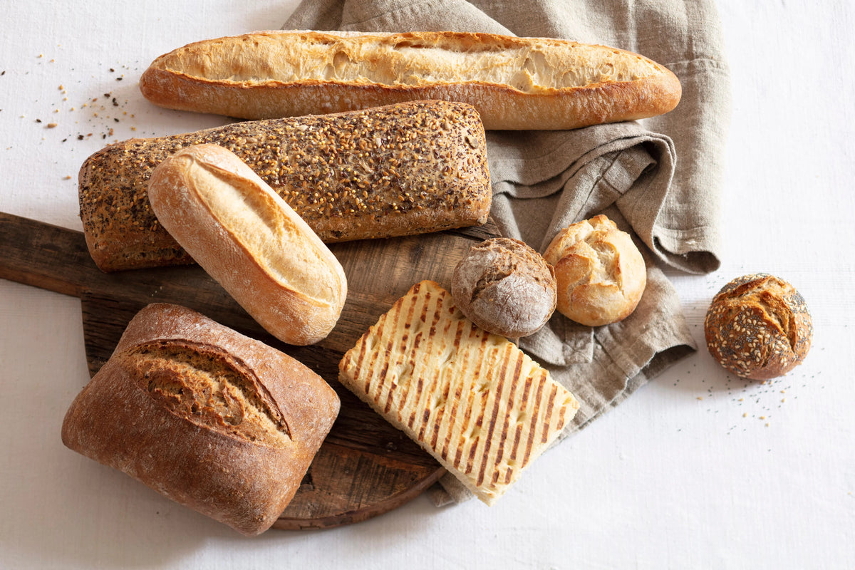 Selection of Delifrance artisan breads including baguette, multigrain loaf, rolls, and panini on a wooden board