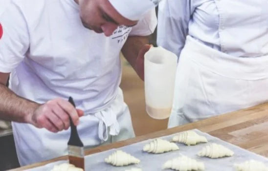 Delifrance pastry chef glazing croissants in a professional kitchen during preparation process
