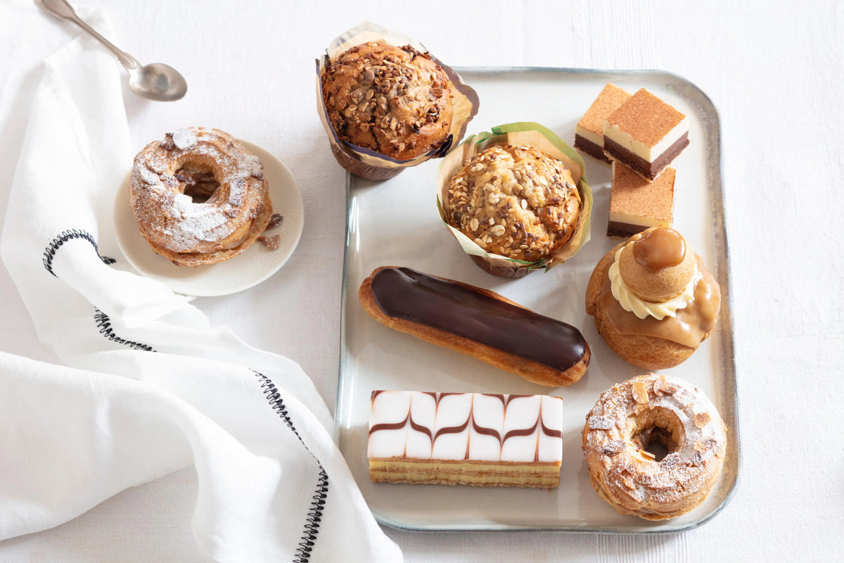 Assorted Delifrance French pastries and desserts including eclair, mille-feuille, muffins, and cream puffs on a tray