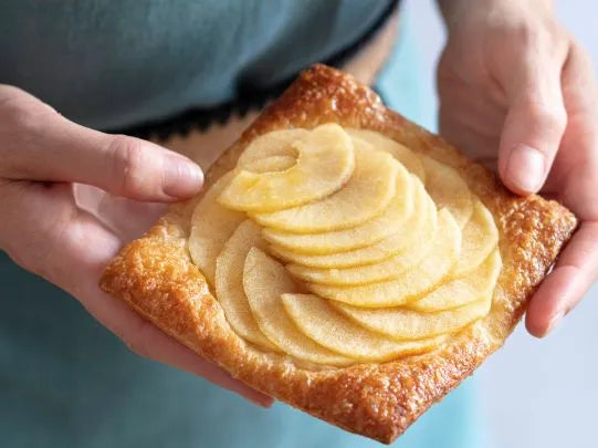 Glazed apple tart held by hand, highlighting food styling shine and portion focus to improve bakery business presentation value